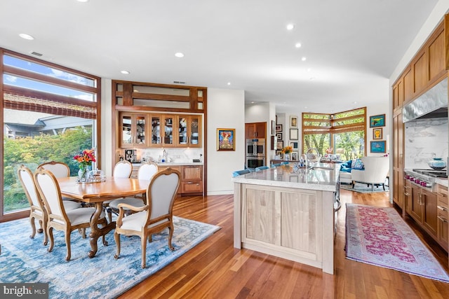 kitchen featuring decorative backsplash, light wood-type flooring, a center island with sink, double oven, and sink