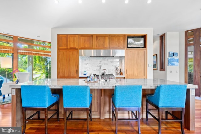 kitchen with a spacious island, backsplash, dark hardwood / wood-style flooring, and light stone counters