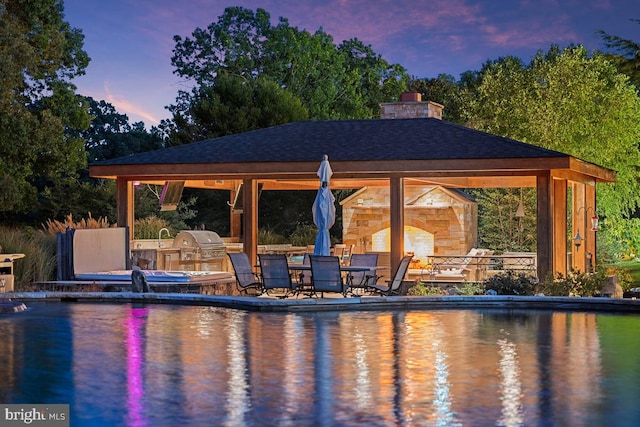 pool at dusk featuring a patio, a gazebo, area for grilling, and exterior kitchen