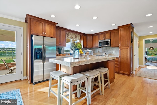 kitchen with light wood-type flooring, light stone counters, a kitchen breakfast bar, appliances with stainless steel finishes, and crown molding