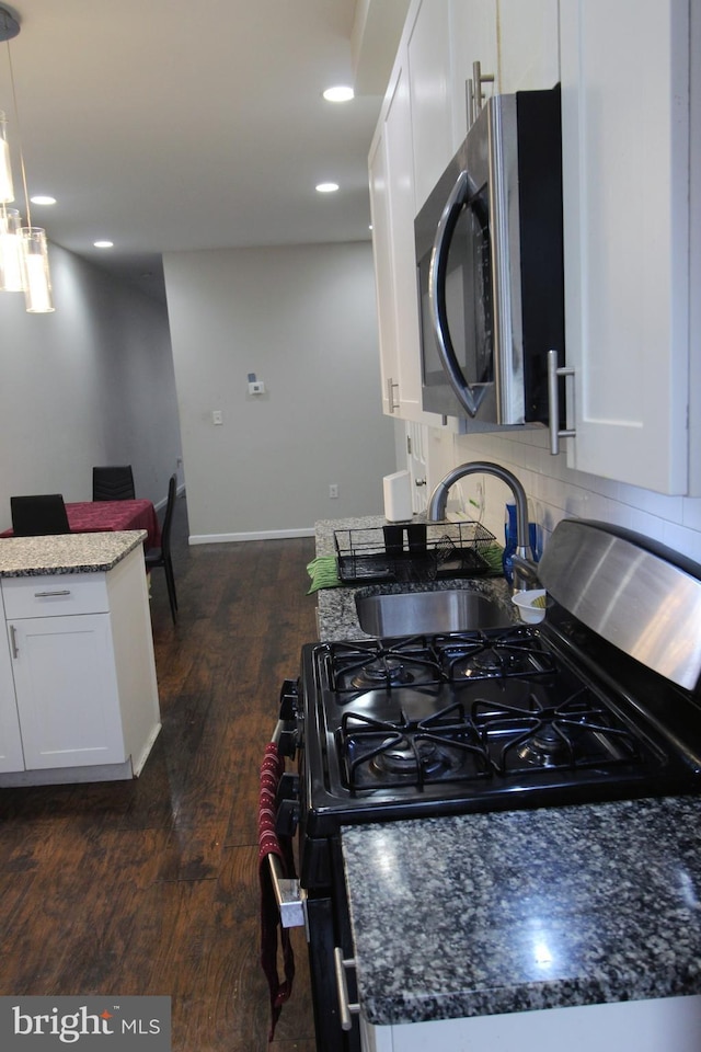 kitchen with dark wood-type flooring, dark stone countertops, hanging light fixtures, gas stove, and white cabinets