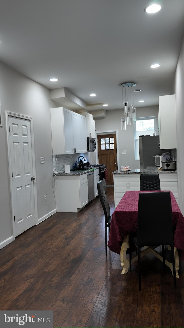 kitchen with hanging light fixtures, white cabinets, stainless steel appliances, light stone countertops, and backsplash