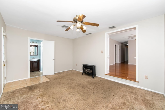 unfurnished living room with ceiling fan, carpet floors, a wood stove, and visible vents