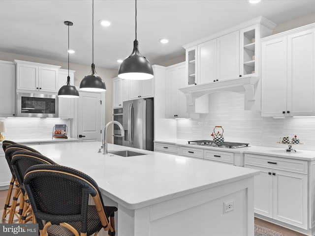 kitchen with pendant lighting, sink, a center island with sink, stainless steel appliances, and a breakfast bar area