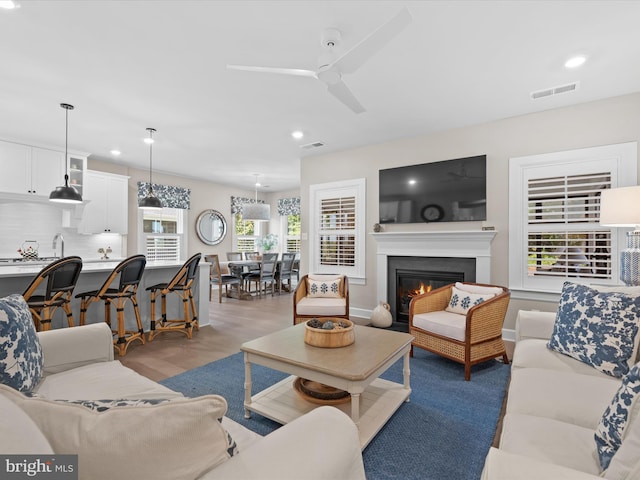 living room featuring light hardwood / wood-style flooring, ceiling fan, plenty of natural light, and sink