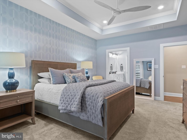 carpeted bedroom with crown molding, a tray ceiling, ceiling fan, and ensuite bathroom