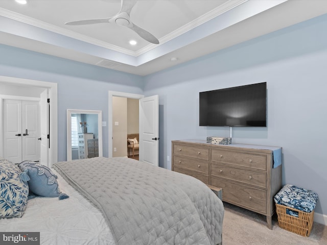 bedroom with ceiling fan, ornamental molding, a tray ceiling, light colored carpet, and ensuite bath