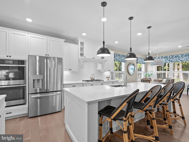 kitchen featuring appliances with stainless steel finishes, hanging light fixtures, a kitchen island with sink, and sink