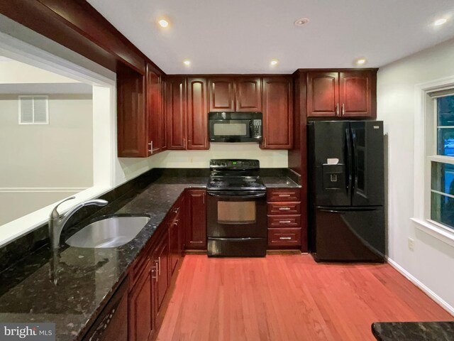 kitchen with light wood-type flooring, black appliances, dark stone countertops, and sink