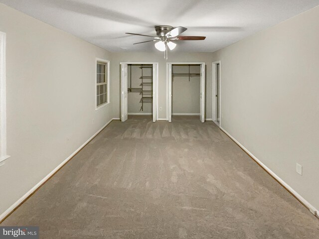 unfurnished bedroom featuring ceiling fan, multiple closets, and carpet floors