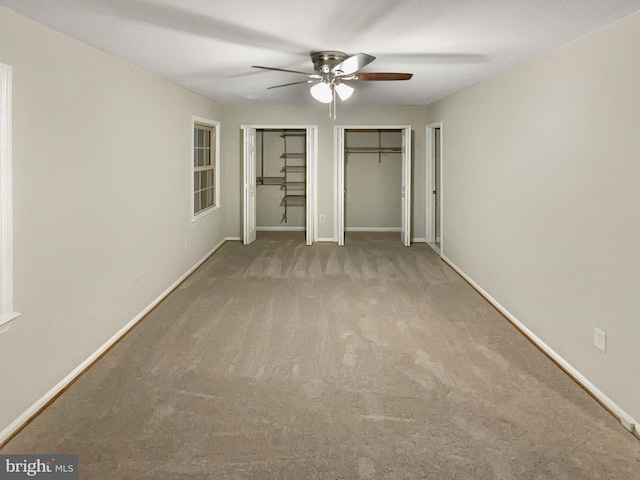 unfurnished bedroom with ceiling fan, baseboards, carpet flooring, and two closets