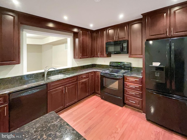 kitchen with light wood-type flooring, dark brown cabinets, black appliances, dark stone counters, and a sink