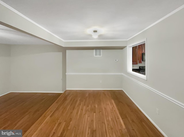 spare room with crown molding, visible vents, baseboards, and wood finished floors