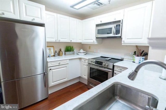 kitchen with white cabinets, appliances with stainless steel finishes, light stone counters, dark hardwood / wood-style flooring, and sink