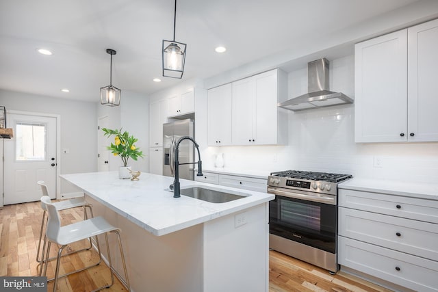 kitchen featuring stainless steel appliances, an island with sink, wall chimney exhaust hood, white cabinets, and light hardwood / wood-style floors