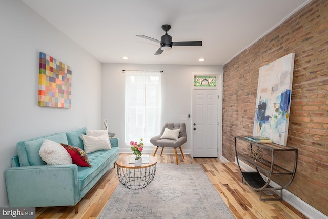 living room featuring light hardwood / wood-style flooring, ceiling fan, and brick wall