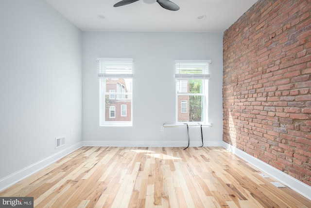 empty room with brick wall, ceiling fan, and light hardwood / wood-style floors