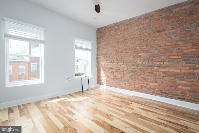 empty room featuring brick wall, ceiling fan, and light wood-type flooring