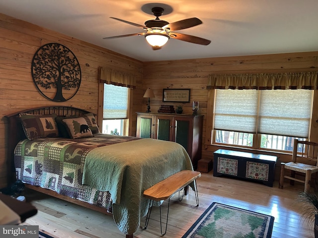 bedroom with light hardwood / wood-style flooring, wooden walls, multiple windows, and ceiling fan