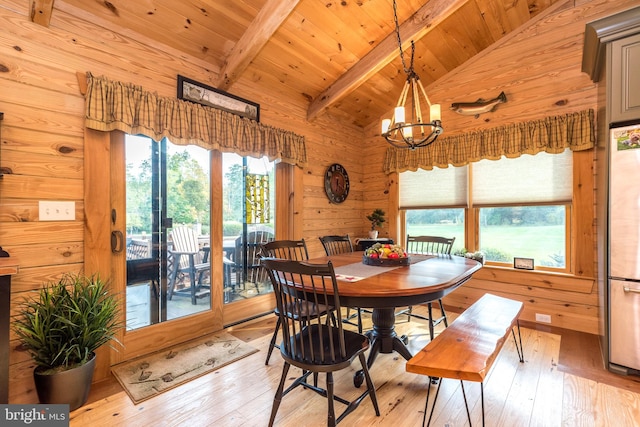 dining space featuring wood walls, light hardwood / wood-style floors, lofted ceiling with beams, and an inviting chandelier