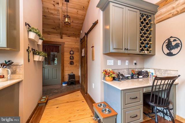 kitchen with built in desk, gray cabinetry, light hardwood / wood-style floors, vaulted ceiling, and wood walls