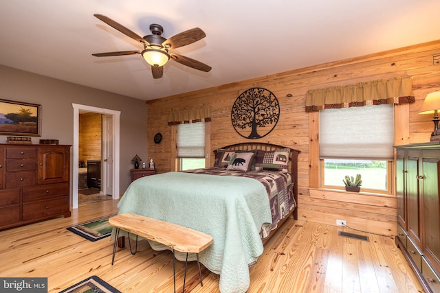 bedroom with ceiling fan, light hardwood / wood-style flooring, and wood walls