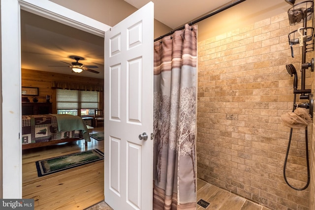 bathroom featuring ceiling fan, wooden walls, wood-type flooring, and a shower with shower curtain