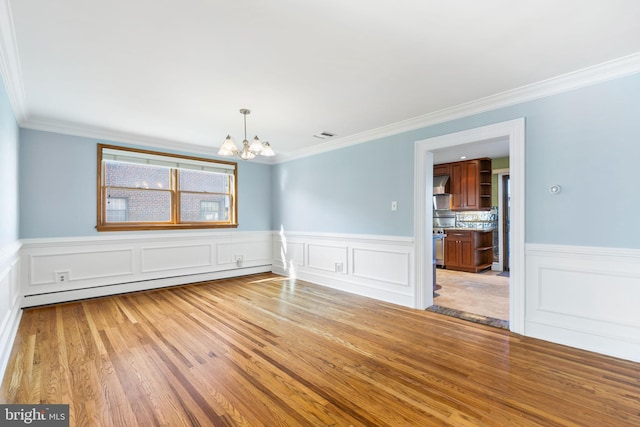 spare room featuring crown molding, baseboard heating, an inviting chandelier, and light wood-type flooring