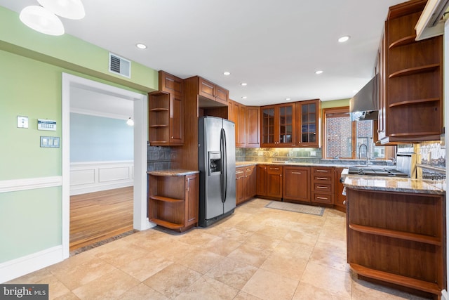 kitchen with dark stone countertops, stainless steel fridge, backsplash, exhaust hood, and kitchen peninsula