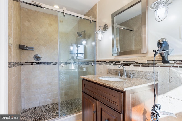 bathroom with vanity, tile walls, a shower with shower door, and decorative backsplash