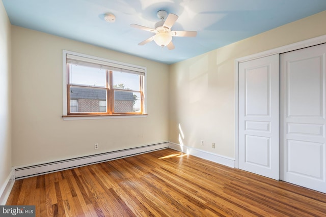 unfurnished bedroom featuring baseboard heating, a closet, ceiling fan, and hardwood / wood-style flooring