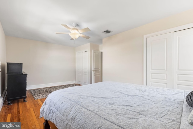 bedroom featuring hardwood / wood-style floors, ceiling fan, and multiple closets