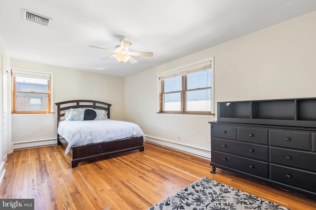 bedroom with baseboard heating, ceiling fan, multiple windows, and light hardwood / wood-style floors