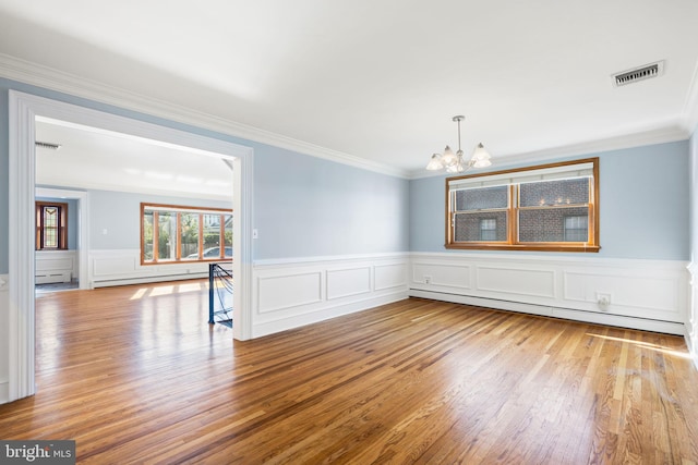 spare room featuring light wood-type flooring, a baseboard heating unit, a chandelier, and ornamental molding