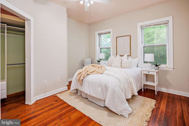 bedroom with dark hardwood / wood-style flooring, ceiling fan, radiator heating unit, and multiple windows