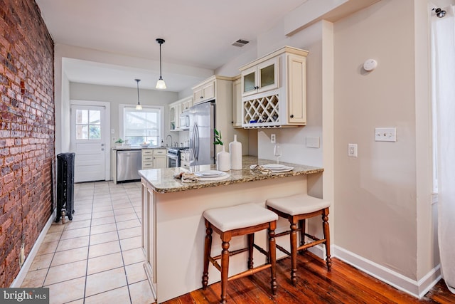 kitchen featuring light wood-type flooring, appliances with stainless steel finishes, decorative light fixtures, and kitchen peninsula