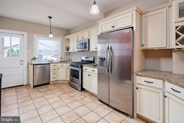 kitchen with decorative light fixtures, stainless steel appliances, sink, cream cabinetry, and light stone counters