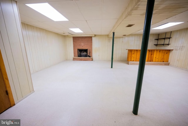 basement featuring a drop ceiling, a brick fireplace, and wooden walls