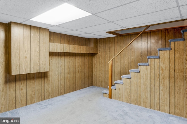 basement featuring a paneled ceiling, carpet floors, and wooden walls