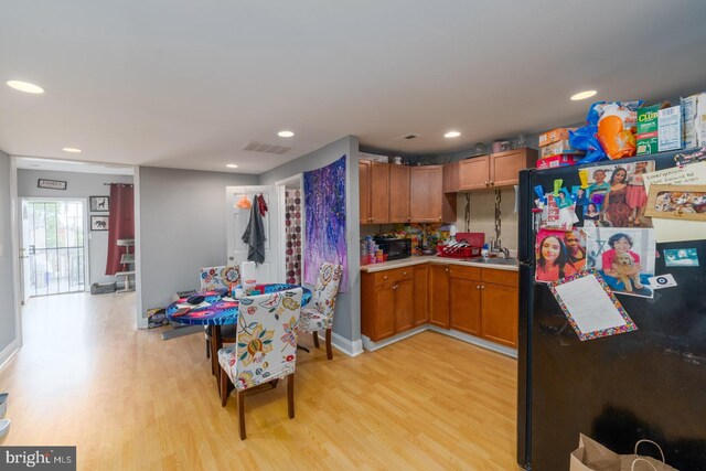 kitchen featuring light hardwood / wood-style flooring, decorative backsplash, black refrigerator, and sink