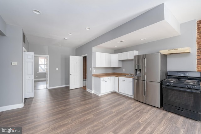 kitchen with black gas stove, stainless steel fridge, white cabinetry, and hardwood / wood-style floors