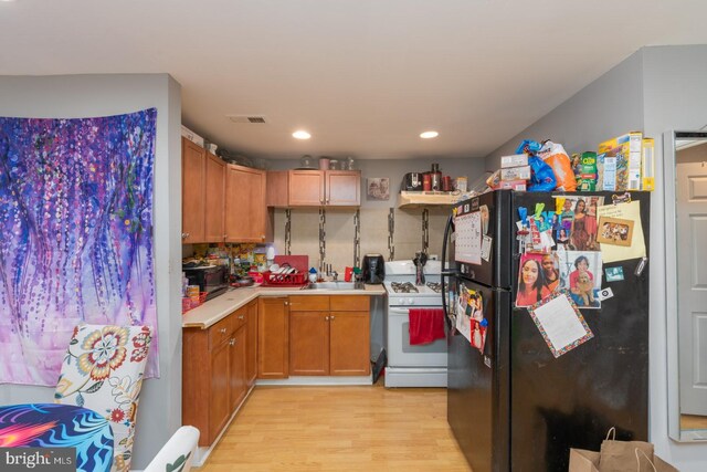 kitchen featuring sink, light wood-type flooring, black refrigerator, and white gas range oven