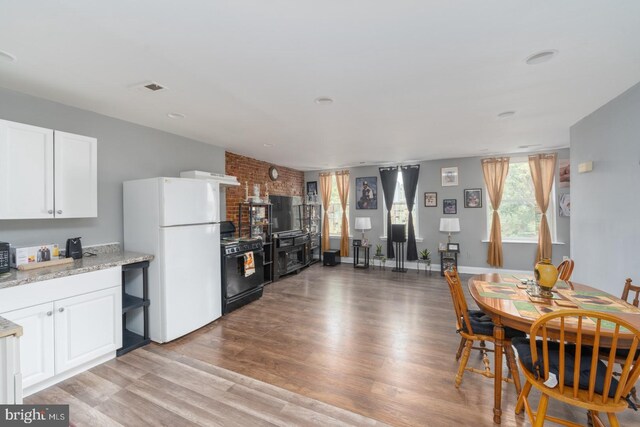 kitchen featuring light stone counters, white cabinets, light hardwood / wood-style flooring, black / electric stove, and white fridge