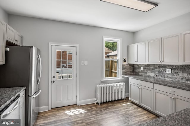 kitchen featuring stainless steel appliances, radiator, backsplash, and light hardwood / wood-style floors