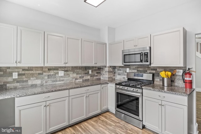 kitchen featuring tasteful backsplash, light hardwood / wood-style flooring, stainless steel appliances, light stone counters, and white cabinets