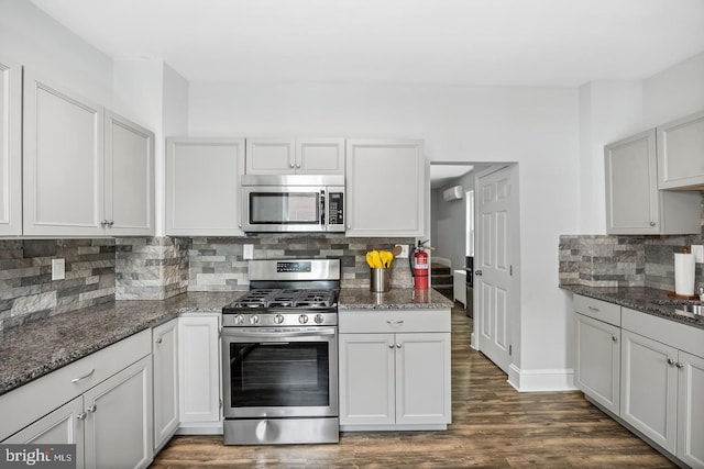 kitchen featuring dark stone countertops, baseboards, dark wood-style flooring, appliances with stainless steel finishes, and backsplash