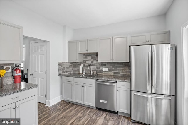 kitchen with dark stone countertops, appliances with stainless steel finishes, sink, dark wood-type flooring, and decorative backsplash