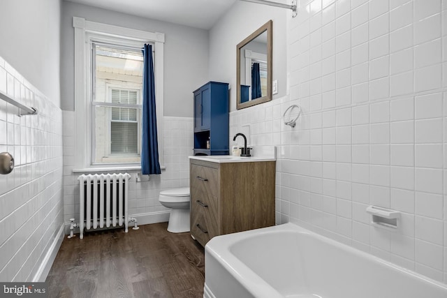 bathroom with toilet, vanity, radiator, tile walls, and hardwood / wood-style flooring