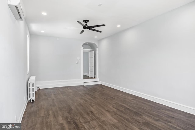 empty room with radiator, a wall mounted AC, recessed lighting, arched walkways, and dark wood-type flooring