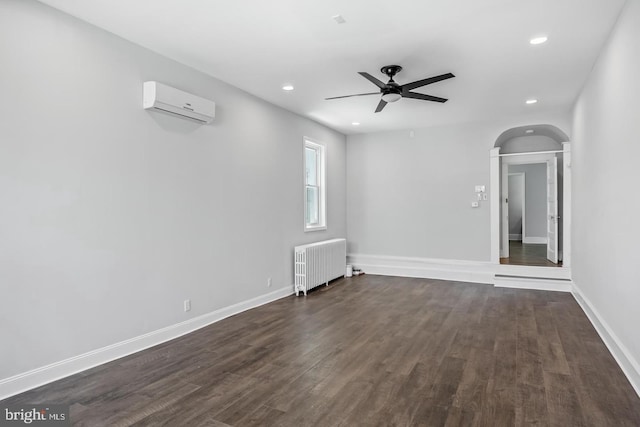 spare room with radiator, dark hardwood / wood-style flooring, a wall mounted air conditioner, and ceiling fan